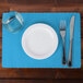A white plate with a fork, knife, and glass on a blue Marina scalloped paper placemat.