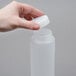 A hand holding a white plastic bottle with a white plastic cap.
