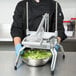 A person in a chef's uniform using a Nemco Easy Lettuce Cutter to chop lettuce.