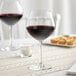 Two Acopa burgundy wine glasses on a table with a glass of red wine.