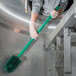 A person in gloves cleaning a stainless steel sink with a Carlisle green brush with a green handle.
