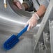 A person in gloves cleaning a metal surface with a blue Carlisle Sparta brush with a handle.