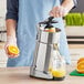 A person in a blue apron using a Ceado SL98 commercial electric citrus juicer to make orange juice.