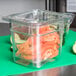 A Cambro clear plastic colander pan filled with cucumbers and vegetables on a counter.