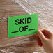 A hand holding a "Skid Of" label.