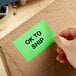 A hand holding a green Lavex Matte Paper label sticker on a cardboard box.