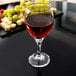 A Libbey wine glass filled with red wine and grapes on a table.