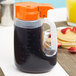 A Tablecraft plastic dispenser jar with an orange lid filled with black liquid.