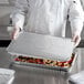 A chef holding a full size foil steam table pan lid filled with food.