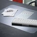 A desk with a clear Artistic KrystalView desk pad with a keyboard and papers.