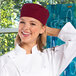 A woman wearing a Uncommon Burgundy Chef Skull Cap with Hook and Loop Closure smiling in a professional kitchen.