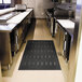 A black Guardian Free Flow Comfort Utility floor mat in a kitchen with stainless steel appliances.