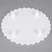 A white round Wilton cake separator plate with scalloped edges and holes in it.
