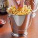 A person holding a Vollrath mini stainless steel bucket filled with french fries.
