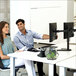 A man and woman sitting at a desk with two Fellowes black horizontal dual monitor arms.