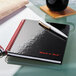 A close-up of a Black n' Red matte black notebook with a pen on it.