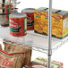 A metal wire shelf with Alera clear plastic liner holding canned food and boxes.