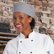 A woman wearing a Uncommon Chef houndstooth chef skull cap smiling in a professional kitchen.