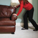A woman in a red sweater and black pants using Master Caster Mighty Mighty Movers to push a brown leather couch.