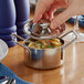 A hand holding a Vollrath mini stainless steel casserole dish with food in it.