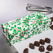 A 1-piece holly holiday candy box with chocolates inside on a counter.