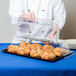 A chef opening a clear Cal-Mil rectangular tray cover to reveal pastries.