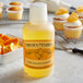 A bottle of Nielsen-Massey Pure Orange Extract next to cupcakes with orange topping.