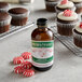 A bottle of Nielsen-Massey Pure Organic Peppermint Extract next to chocolate cupcakes with a peppermint candy on top.