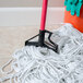 A red Carlisle mop handle cleaning up a pile of white string.