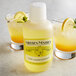 A bottle of Nielsen-Massey Pure Lemon Extract on a counter with two glasses of lemonade.
