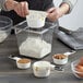 A woman uses OXO white measuring cups with black handles to measure flour into a bowl.