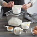 A woman using white OXO measuring cups to pour flour into a bowl.