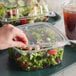 A hand putting salad in a Dart ClearPac plastic container.