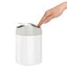A hand opening a white simplehuman stainless steel countertop trash can.