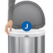 A person holding a blue and white box of simplehuman custom fit trash can liners with a white circle and J in the middle.