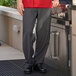 A man in a red shirt wearing Uncommon Chef black and gray houndstooth pants standing next to an outdoor grill.