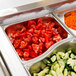 A Vollrath stainless steel food pan with cucumbers and tomatoes on a buffet counter.