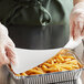 A gloved hand places a foil-laminated board lid on a foil container of french fries.
