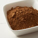 A bowl of brown Regal Ground Allspice powder on a white surface.