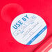 A red plastic container with a white Noble Products round "Use By" label.