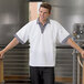 A man wearing a white Uncommon Chef cook shirt with Shepherd's check trim standing in a room.