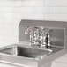 A stainless steel deck-mounted faucet with 4-inch centers and a 6-inch swing spout installed on a metal sink.