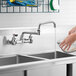 A hand washing a bowl in a sink with a Waterloo wall-mounted faucet.