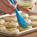 A person using an Ateco flat blue silicone bristle brush to paint food.