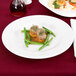 A white Arcoroc porcelain banquet plate with meat and vegetables on it on a table.