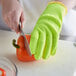 A person wearing yellow Mercer Culinary cut-resistant gloves cutting a red bell pepper.