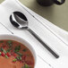 A bowl of soup with an Acopa Phoenix stainless steel bouillon spoon next to it.