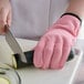 A person wearing a pink Mercer Culinary Millennia Cut-Resistant glove cutting a zucchini with a knife.