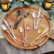 A wooden cutting board with Acopa Phoenix rose gold flatware and candles.