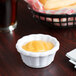 A white Carlisle ramekin filled with yellow sauce on a table.